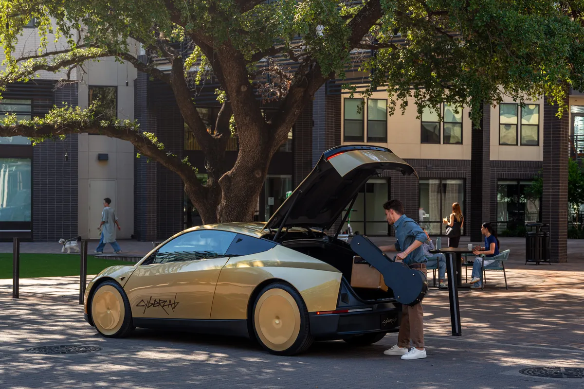 Un homme dépose un sac dans le coffre arrière ouvert d’un Tesla Cybercab stationné devant une résidence.
