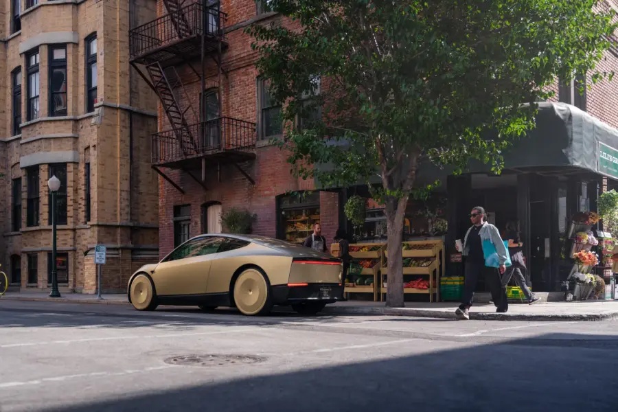 Tesla Cybercab doré stationné le long d’un trottoir dans une rue commerçante, un passant traversant devant lui.